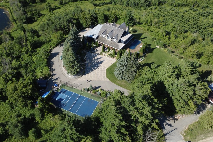 High overhead drone view of the house, courtyard and sport court surrounded by dense woodland