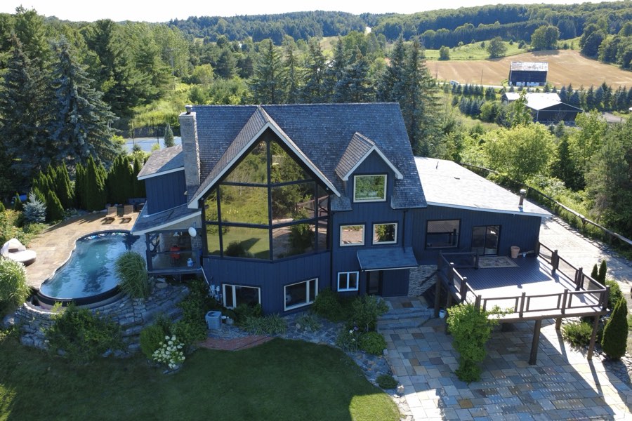 Drone view of the rear of the property showing the two-storey glass gable, decks and curved pool