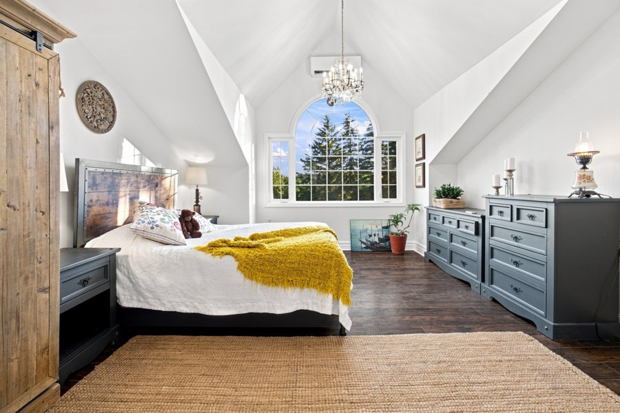 Upper bedroom under a vaulted ceiling with an arched Palladian window and a crystal chandelier