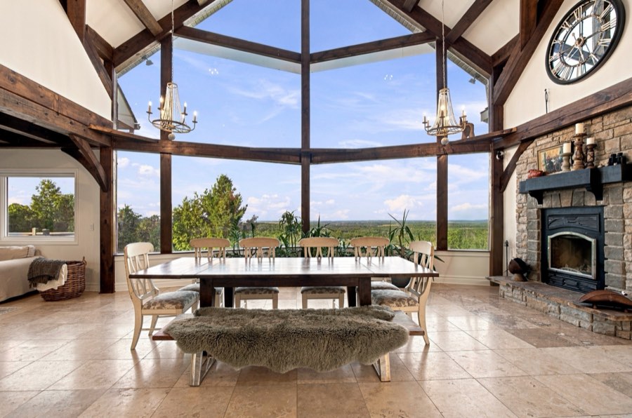 Long dining table beneath twin chandeliers, beside a floor-to-ceiling stone fireplace