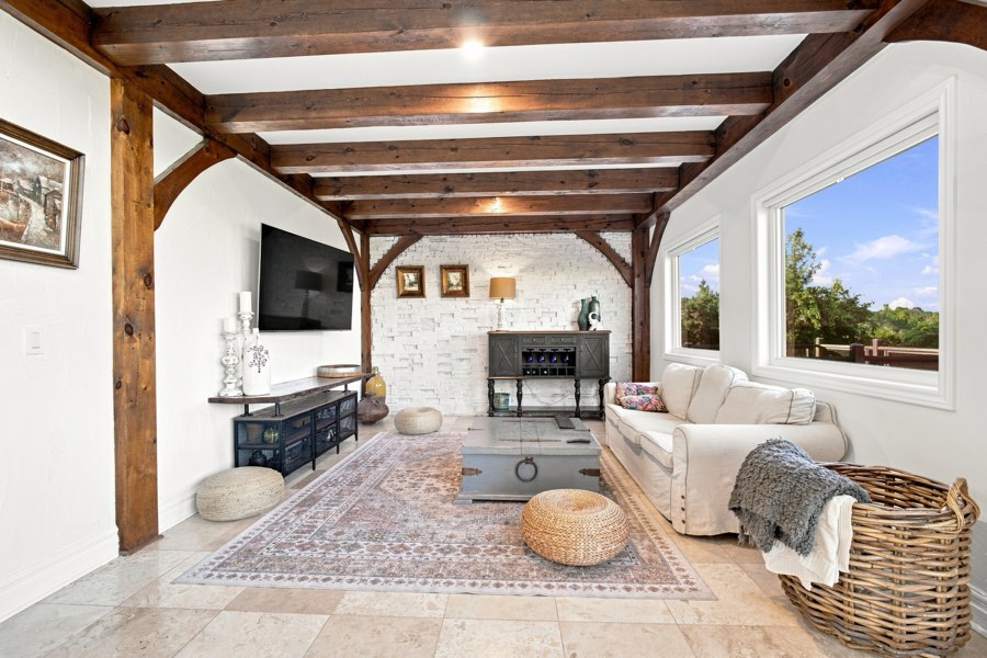 Family room with a close-beamed ceiling, whitewashed brick wall and a pale sofa under a picture window