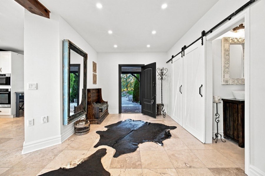 Bright travertine foyer with white sliding barn doors, a hide rug and an oversized leaning mirror
