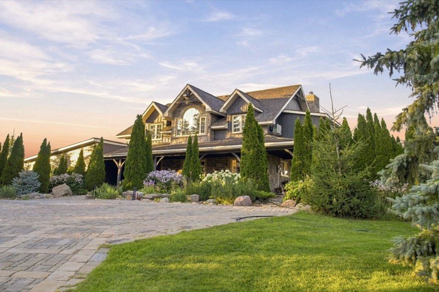 Low evening sun across the front gardens and stone courtyard of a shingled country home