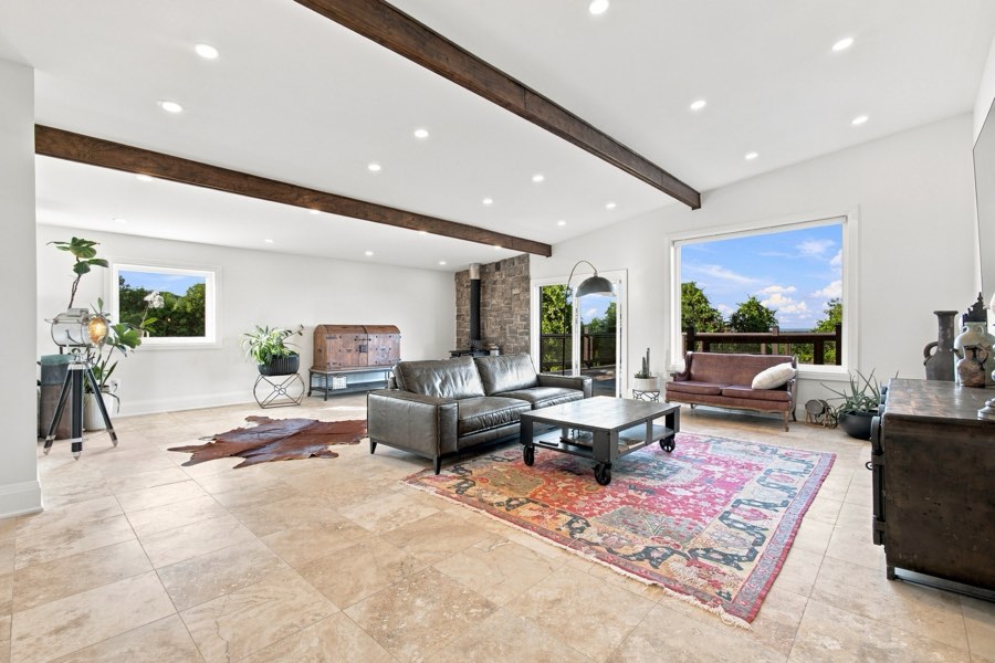 Living room with exposed beams, a stone fireplace and a patterned rug on travertine floors