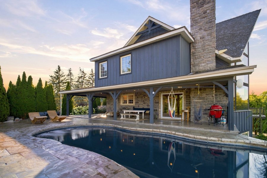 Pool at dusk reflecting the lit stone chimney and covered outdoor kitchen behind it