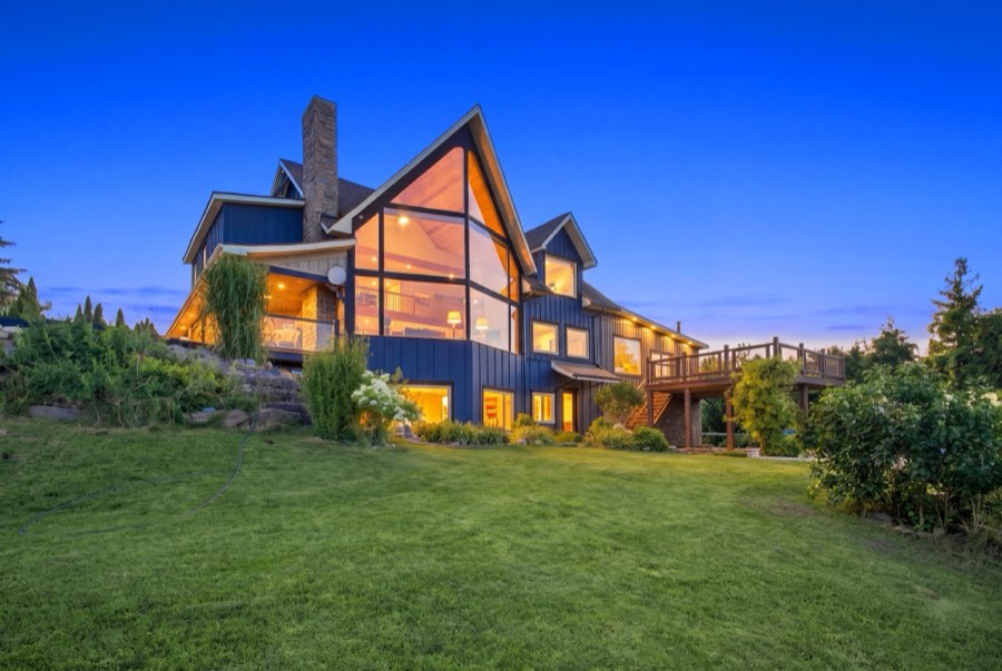 Rear elevation of a timber-frame home at twilight, every window glowing warm against a deep blue sky