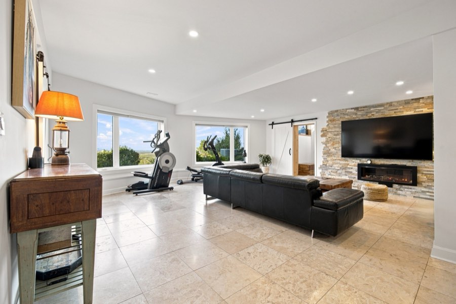 Lower-level recreation room with a linear fireplace set in stacked stone and a wall of windows