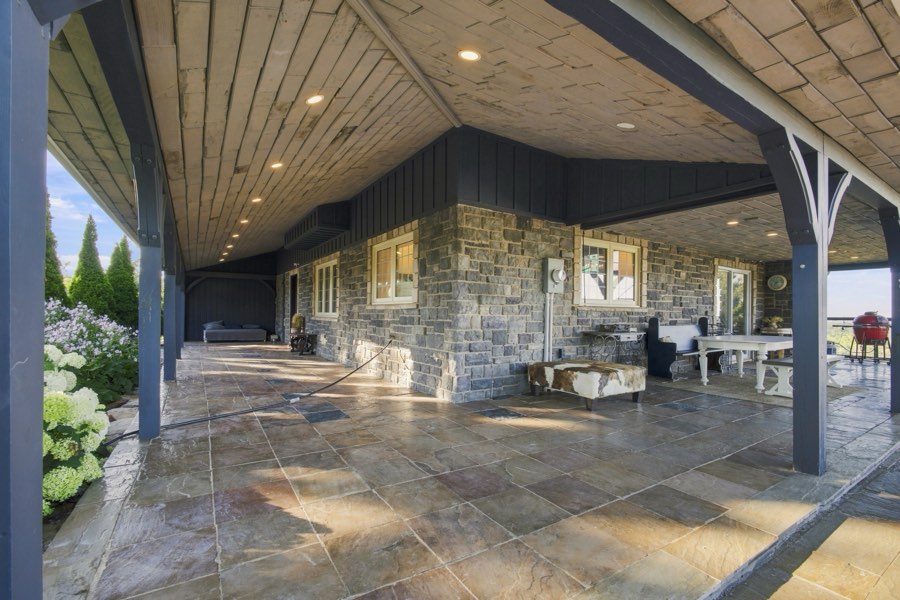 Long covered loggia with a plank ceiling, stone walls and flagstone floor running the length of the house